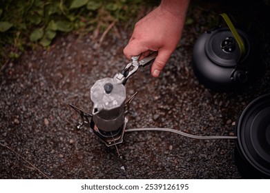 Close-up of a hand using pliers to adjust a moka pot on a portable camping stove. Ideal for camping, coffee brewing, and outdoor lifestyle themes.  - Powered by Shutterstock