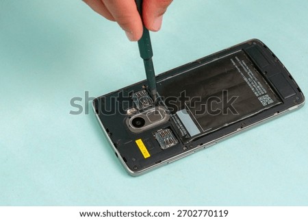Close-up of a hand using a precision screwdriver to work on the internal components and SIM card slots of a disassembled smartphone. Technical mobile repair