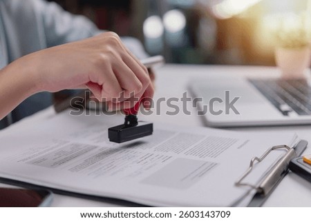Close-up of hand using a red stamp on a legal document, indicating confirmation or validation in administrative work.