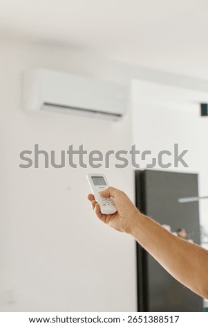 Close-up of hand using remote control to adjust temperature on wall-mounted air conditioner. Concept of indoor climate control and cooling during hot weather