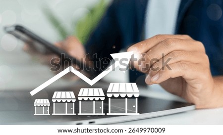 Close-up of a hand using a smartphone with increasing store graph icons, representing franchise business growth, retail expansion, and multi-location store strategy.