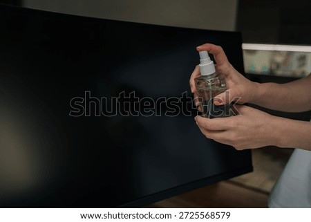 Close-up of hand using soft cloth to carefully clean top and side edge of dark computer monitor, performing routine technology maintenance for clean workspace.