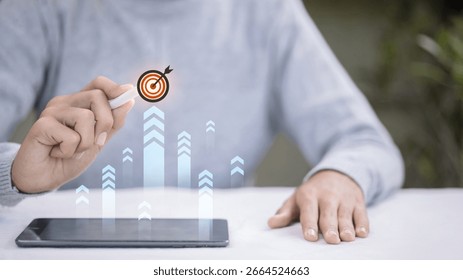 Close-up of a hand using a tablet with a virtual target icon and upward arrows, representing business goals, growth, strategy, and success in modern technology and marketing.