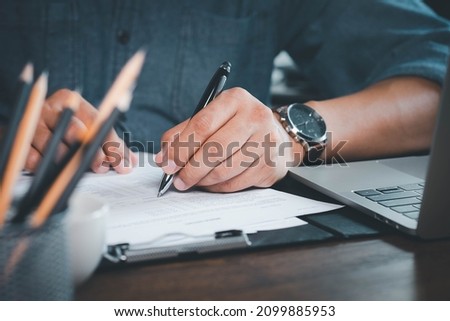 Close-up of Hand using writing pen with questionnaire or paperwork survey question filling in business company personal information form checklist document.