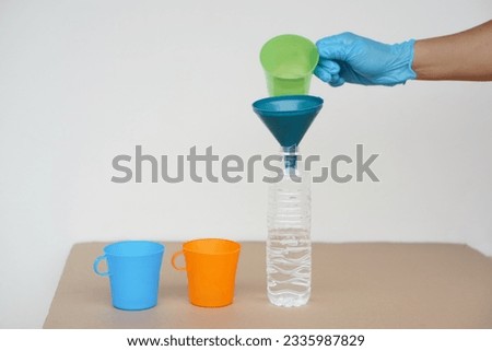 Closeup hand wear blue glove holds green mug to pour water into bottle to do science experiment. Concept, water quantity measurement for mixing chemical substances.            