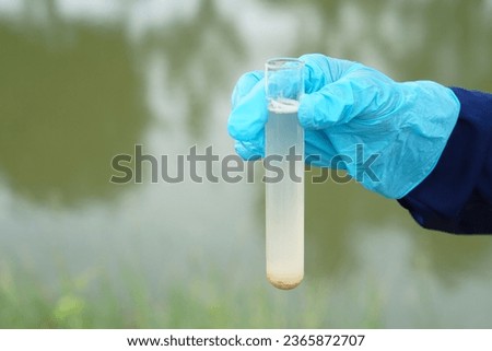 Closeup hand wears blue glove holds test tube of sample water from lake. Concept, explore, inspect quality of water from natural source, prepare for doing experiment. Test of water pollution.         