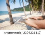 Close-up of hand while applying sunscreen. Skin care during summer vacations on beautiful sand beach with palm trees in tropical destination.