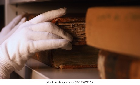 Close-up Of Hand In White Cotton Glove Taking Very Old Book From The Bookshelf In Museum Or Private Library. Stock Footage. Exploring Of The Ancient Yellowed Books