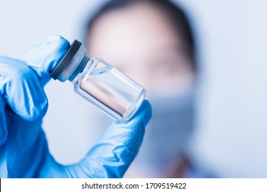 Closeup hand of woman doctor or scientist in doctor's uniform wearing face mask protective in lab holding medicine liquid vaccines vial bottle, coronavirus or COVID-19 concept, studio shot isolated