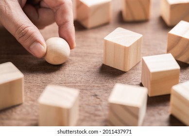 Closeup hand and wood sphere, try to find the right position to place it down among the cutting wood cubes, position in the market, business concept - Shutterstock ID 2011437971