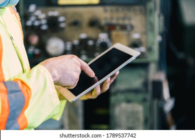 Closeup Hand Worker In Protective Safety Jumpsuit Uniform With Yellow Hardhat And Using Tablet At Factory.Metal Working Industry Concept Professional Engineer Manufacturing 