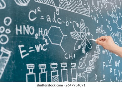 Close-up of hand writing chemical formulas and atomic structure using chalk on blackboard. Represents science education, chemistry class, research, and learning in academic or laboratory environment.