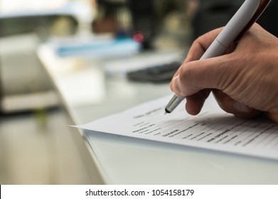 Closeup of hand writing filling job or service application form over light desk background. Signing with pen checklist, college student or education university program certificate. Business contract - Powered by Shutterstock