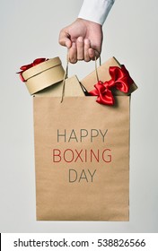 Closeup Of The Hand Of A Young Caucasian Man Holding A Paper Shopping Bag Full Of Gifts And The Text Happy Boxing Day Written In It