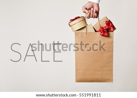 closeup of the hand of a young caucasian man holding a paper shopping bag full of gifts and the word sale