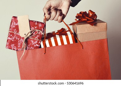 closeup of the hand of a young caucasian woman with her fingernails painted red holding a red shopping bag full of gifts wrapped in different papers