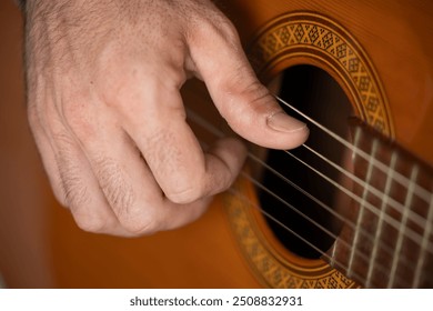 Close-up hand of young handsome male musician playing classical Spanish guitar concentrated on the sofa in the living room of his home, playing blues, flamenco, jazz or rock and roll alone - Powered by Shutterstock