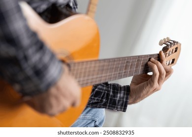 Close-up hand of young handsome male musician playing classical Spanish guitar concentrated on the sofa in the living room of his home, playing blues, flamenco, jazz or rock and roll alone - Powered by Shutterstock