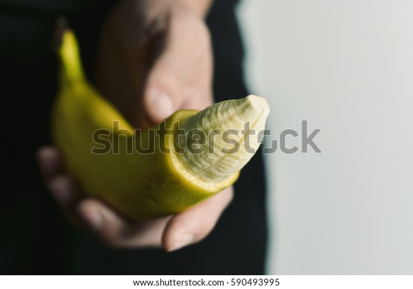 closeup of
the hand of a young man with a banana with the tip of its skin
removed, depicting a circumcised male
member