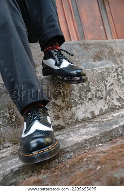 Close-up of handcrafted twotone\
black-and-white brogue-wingtip shoes made of genuine leather with\
rubber soles worn by a man to sit on the stairs\
outdoors