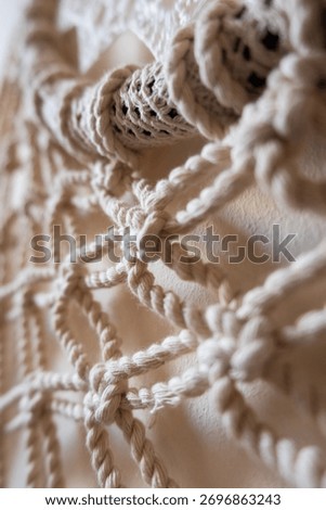 Close-up of a handmade macrame wall hanging. The intricate knots and patterns are visible, showcasing the craftsmanship and texture of the natural fibers.