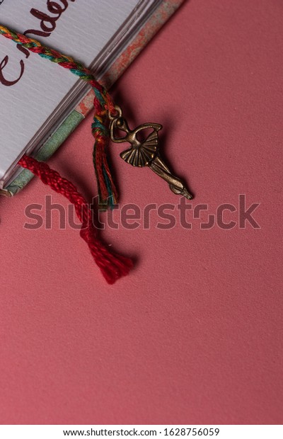 Close-up of handmade\
notebook dividers with braided thread with copper dancer on the\
tip, on a pink table