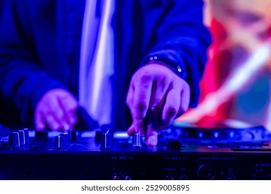 Close-up of hands adjusting knobs on DJ mixer with colorful blurred lights in the background, capturing the vibrant energy of live music event. Perfect for nightlife, music, and entertainment themes. - Powered by Shutterstock