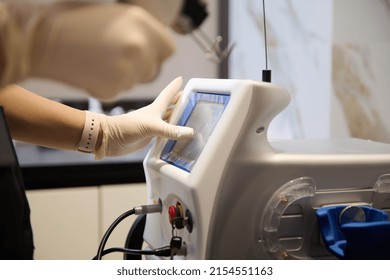 Close-up Of The Hands Of An Aesthetician In A Black Uniform Holding A Laser Resurfacing Machine And Pointing With Finger At The Monitor Screen And Adjusting Programs On A Hardware Beauty Apparatus