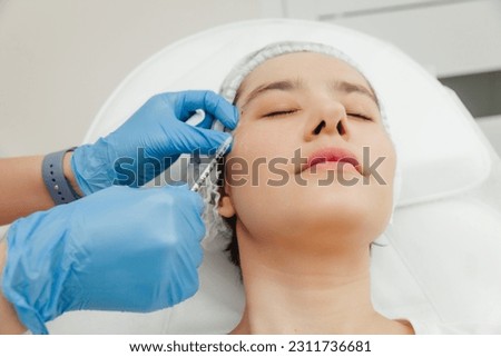 Close-up of the hands of a beautician injecting Botox into a woman's forehead. Correction of forehead and eye wrinkles with botulinum toxin.