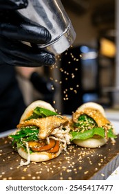 Close-up of a chef’s hands in black gloves assembling gourmet bao buns with fresh ingredients on a wooden surface. The image highlights the preparation of high-quality street food