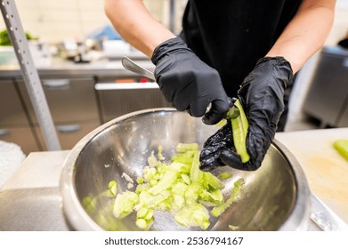 Close-up of hands in black gloves slicing green vegetables in a stainless steel bowl. The image captures the precision and care in food preparation, highlighting the freshness of the ingredients. - Powered by Shutterstock