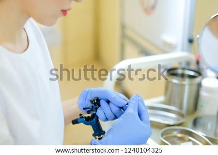 Closeup hands in blue latex gloves inserting needle into microblading machine at beauty salon. Concept of cosmetology equipment for permanent makeup.