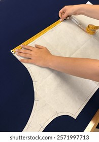 Close-up of hands carefully measuring a pattern on fabric with a measuring tape. The image captures the meticulous process of preparing materials for sewing and garment construction with precision