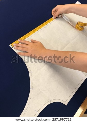 Close-up of hands carefully measuring a pattern on fabric with a measuring tape. The image captures the meticulous process of preparing materials for sewing and garment construction with precision