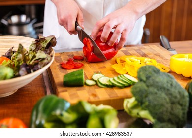 Closeup of hands of chef cook cutting red bell pepper for salad on wooden table - Shutterstock ID 428983537