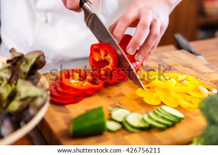 Closeup of hands of chef cook cutting vegetables on wooden table 