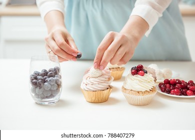 Closeup hands of chef decorating cupcakes with colored berries