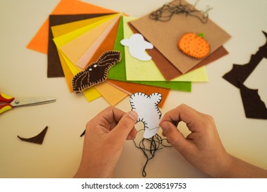 Close-up Of The Hands Of A Child Who Makesdecorative Garland For Halloween From Felt Greetings And Fun. Children Art Project. DIY Concept.