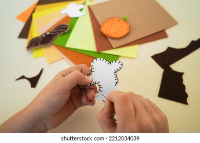 Close-up Of The Hands Of A Child Who Makesdecorative Garland For Halloween From Felt Greetings And Fun. Children Art Project. DIY Concept.