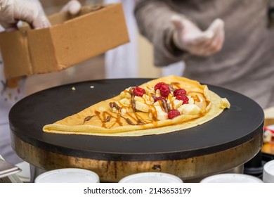 Close-up Of Hands Of Cook In Gloves Preparing Crepe, Pancake On Frying Pan With Fresh Banana, Raspberry, Sweet Sauce, Nutella. Concept National Food, Healthy Fast Food, Summer Paty