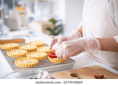 Closeup of hands in cooking gloves decorating freshly baked tart with blueberries strawberry fresh fruit.housewife baker wear apron making fruit tart. homemade bakery at home. - Powered by Shutterstock