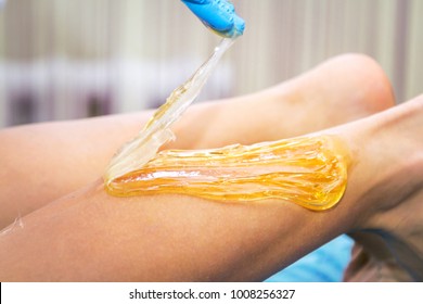 Close-up hands of cosmetologist in blue gloves applying paste for sugaring depilation on female leg , hair removal beauty procedure.