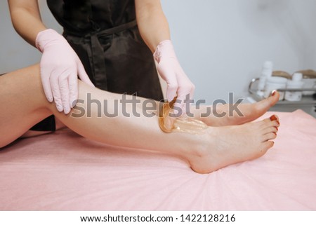 Close-up hands of cosmetologist in gloves applying paste for sugaring depilation on leg, hair removal beauty procedure.
