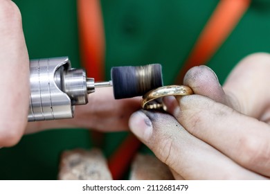 Closeup hands of craftsman jeweler polishing a golden ring surface with grinding machine. Goldsmith is in process of working. - Shutterstock ID 2112681479
