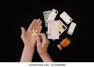 Close-up, The Hands Of Elderly Woman On A Black Background Are Sorting Out Medicines. Lots Of Different Pills. The Concept Of A Large Number Of Diseases In Old Age, Drug Treatment, Age-related Changes