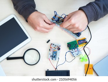Close-up hands with electronics development board. Microcontrollers, chips, resistors, usb cables and notebook on  desktop of hardware engineer. Engineer workplace