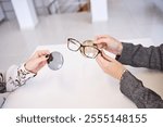 Close-up of hands examining eyeglass frames and interchangeable lenses during a professional eyewear consultation on a bright table.