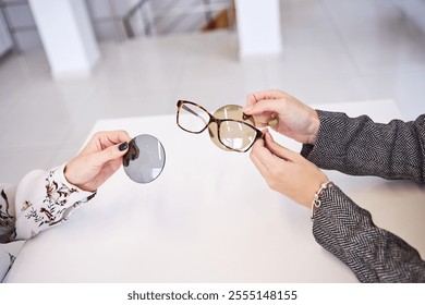 Close-up of hands examining eyeglass frames and interchangeable lenses during a professional eyewear consultation on a bright table.