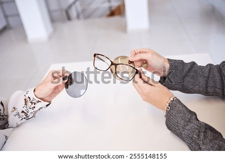 Close-up of hands examining eyeglass frames and interchangeable lenses during a professional eyewear consultation on a bright table.
