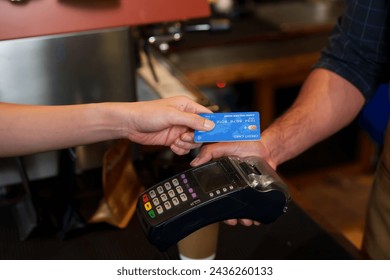 Close-up of hands exchanging credit card and electronic payment terminal over cafe counter. card transaction in progress, showing interaction between customer, barista, and POS machine. - Powered by Shutterstock